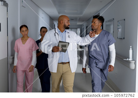 Diverse doctors using tablet and discussing work in corridor at hospital Diverse doctors using tablet and discussing work in corridor at hospital 105972762