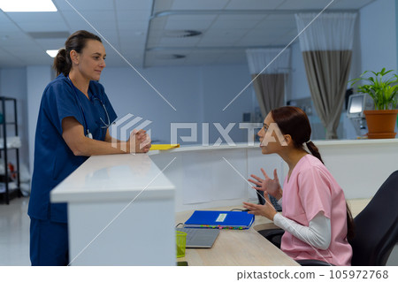 Happy diverse female doctors wearing scrubs talking at reception desk at hospital 105972768