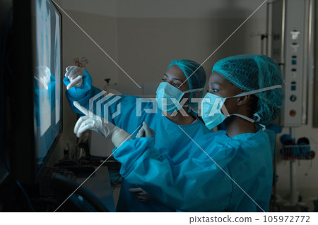 Diverse female surgeons looking at x-ray scans in operating theatre at hospital 105972772