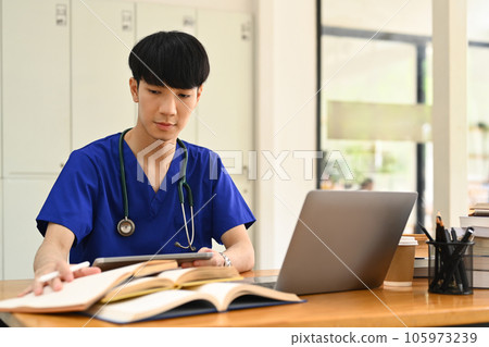 Concentrated male medical student watching online lecture on laptop. Medical internship concept. Concentrated male medical student watching online lecture on laptop. Medical internship concept. 105973239