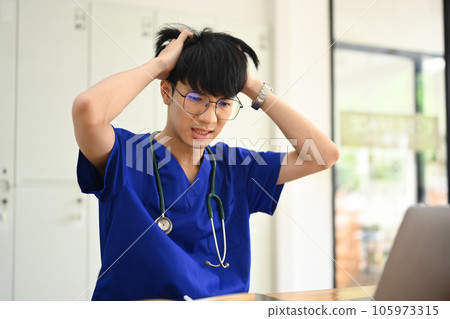 Upset medical student man suffering from headache or feeling tired of studying for college exam. 105973315