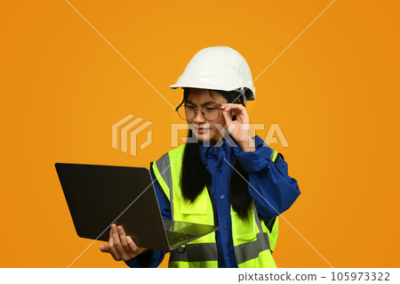Asian girl wearing helmet holding laptop isolated on yellow background, future dream job career as engineer and architect. Asian girl wearing helmet holding laptop isolated on yellow background, future dream job career as engineer and architect. 105973322