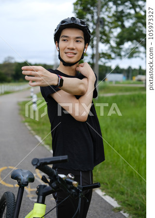 Happy man in sportive outfit and helmet standing near bicycle, stretching arms before cycle workout. Happy man in sportive outfit and helmet standing near bicycle, stretching arms before cycle workout. 105973327