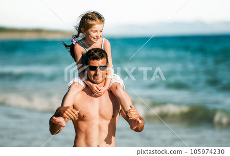 Father holding daughter at shoulders at sea coast portraits. Family dad and little pretty child kid at beach at summer together 105974230