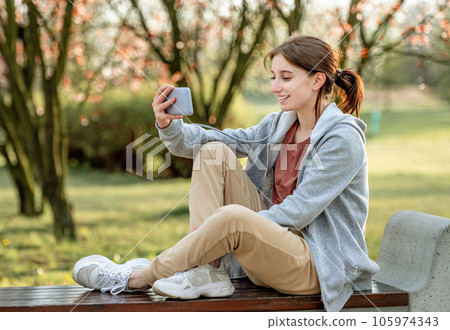 Young girl sitting in the spring park on a bench and having video chat via smartphone 105974343
