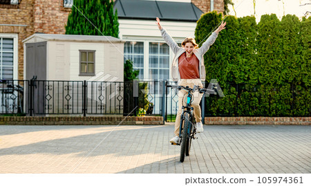 Funny girl riding a bike in the evening with rising hands up. Young girl joking and having fun. Eco-friendly urban transport. Funny girl riding a bike in the evening with rising hands up. Young girl joking and having fun. Eco-friendly urban transport. 105974361