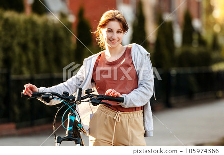 Portrait of cute laughing girl with a bike in the evening in a calm city. Portrait of cute laughing girl with a bike in the evening in a calm city. 105974366