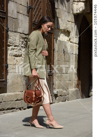 pretty brunette girl in satin long dress ankle strap shoes and checkered jacket posing with leather handbag 105974446