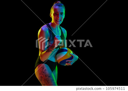 Emotional and motivated young woman, volleyball player cheering up for successful game against black studio background in neon light Emotional and motivated young woman, volleyball player cheering up for successful game against black studio background in neon light 105974511