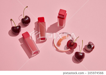 Scene for branding products. Red ripe cherries with lipsticks unbranded arranged on pink background. Cherries contain vitamin C and vitamin B, which help keep lips supple and safe for health 105974566