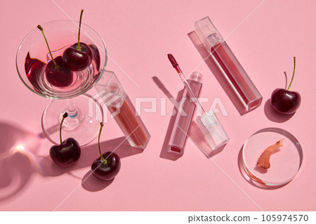 On a pink background, lipsticks unbranded decorated with fresh red ripe cherries and glass cup. Cherry lip balms are an excellent method to keep your lips moisturized and supple On a pink background, lipsticks unbranded decorated with fresh red ripe cherries and glass cup. Cherry lip balms are an excellent method to keep your lips moisturized and supple 105974570
