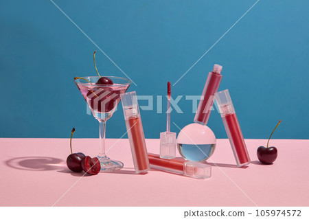 Concept for advertising lipstick with cherry concept. Lipsticks mockup decorated with cherries and glass cup on blue background. Cherries contain vitamin C and vitamin B, which help keep lips supple 105974572