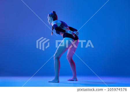 Young woman, professional volleyball player showing game combination with fingers against blue studio background in neon light 105974576