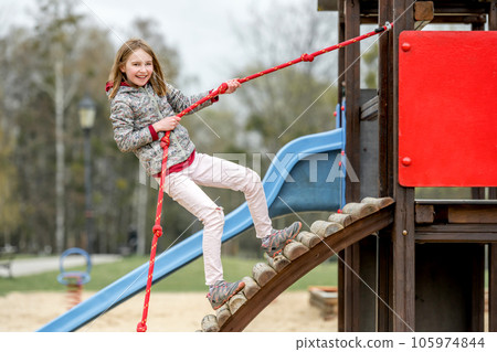 Funny little girl playing in kid's park with rope, smilling and looking into the camera Funny little girl playing in kid's park with rope, smilling and looking into the camera 105974844