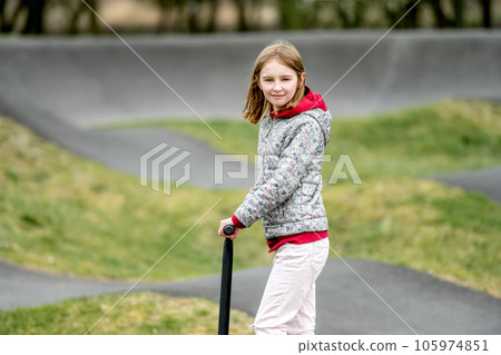 Beautiful little girl rides a scooter in a extreme ride park, smilling and looking into the camera 105974851
