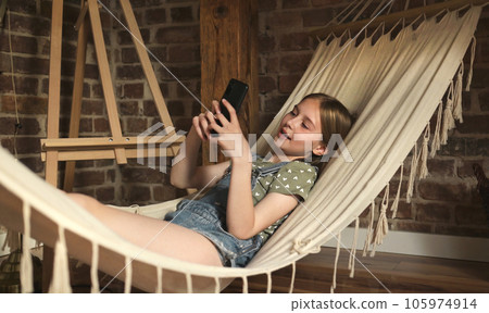 Preteen child girl lying in hammock in loft room at home. Pretty female kid enjoying summer vacation 105974914