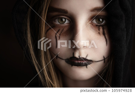 Little girl with spooky Halloween makeup looking at camera closeup portrait. Creepy child kid with crazy joker expression. 105974928