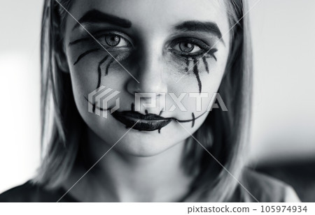 Little girl with spooky Halloween makeup brushed eyes looking at camera. Creepy kid's portrait with crazy joker expression, black and white. Little girl with spooky Halloween makeup brushed eyes looking at camera. Creepy kid's portrait with crazy joker expression, black and white. 105974934