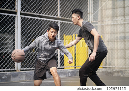 two young asian adult men playing one-on-one basketball on outdoor court 105975135