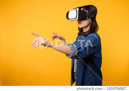 Young asian woman get experienced wearing virtual reality headset game entertainment isolated on yellow background. Winner of cyber future video game concept. 105976067