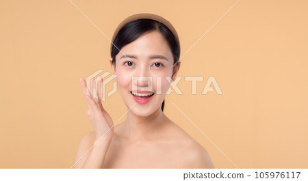 Beautiful girl asian model touching fresh glowing hydrated facial skin on beige background closeup. Beauty face young woman with natural makeup and healthy skin portrait. Skin care concept 105976117
