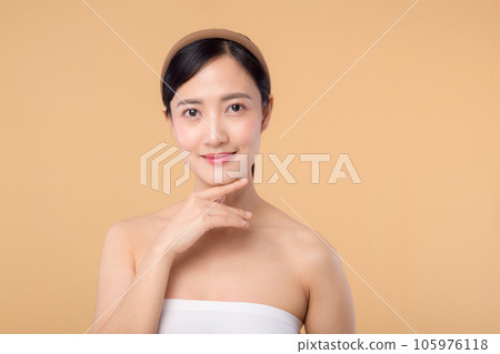 Beautiful girl asian model touching fresh glowing hydrated facial skin on beige background closeup. Beauty face young woman with natural makeup and healthy skin portrait. Skin care concept 105976118
