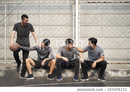 group of four asian young adult men resting relaxing talking chatting on outdoor basketball court 105976152