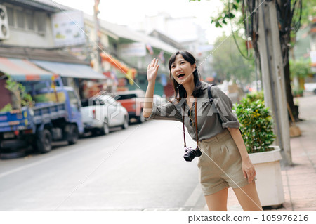 Smiling young Asian woman traveler hitchhiking on a road in the city. Life is a journey concept. Smiling young Asian woman traveler hitchhiking on a road in the city. Life is a journey concept. 105976216