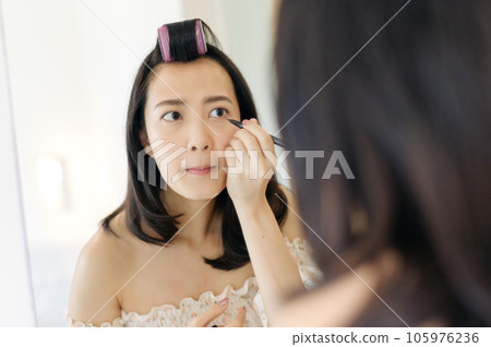 Beautiful young Asian woman applying makeup in front of the mirror. Lifestyle people concept. Advertisement for skin cream, anti-wrinkle cream, baby face Beautiful young Asian woman applying makeup in front of the mirror. Lifestyle people concept. Advertisement for skin cream, anti-wrinkle cream, baby face 105976236