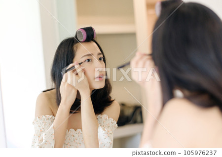 Beautiful young Asian woman applying makeup in front of the mirror. Lifestyle people concept. Advertisement for skin cream, anti-wrinkle cream, baby face Beautiful young Asian woman applying makeup in front of the mirror. Lifestyle people concept. Advertisement for skin cream, anti-wrinkle cream, baby face 105976237