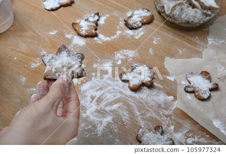 Cooked Christmas cookies in a woman's hand on the background of a table covered with flour.  105977324