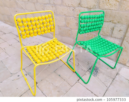 Two chairs are lined up on the marble pavement. Yellow and green empty massage chairs with pimples. Dubrovnik, Croatia. Creative non-standard interior 105977333