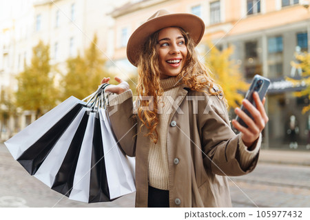 Happy woman with shopping bags walking on street. Purchases, black friday, discounts, sale concept. 105977432