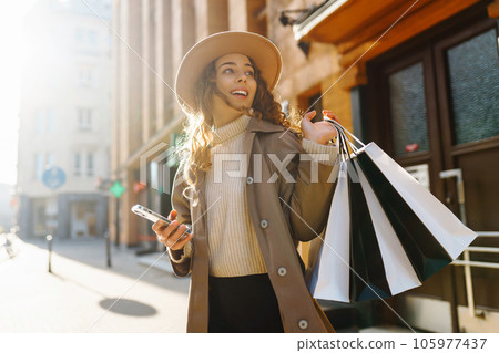 Happy woman with shopping bags walking on street. Purchases, black friday, discounts, sale concept. 105977437