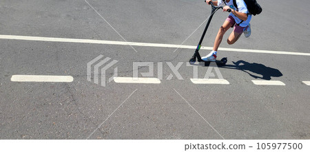 The scooter rides along the track with markings for bicycles, legs are visible. The scooter rides along the track with markings for bicycles, legs are visible. 105977500