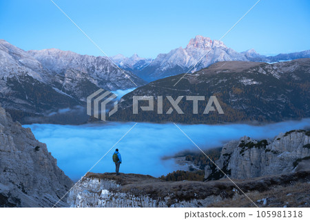 A tourist stands over the fog at the edge of a cliff in the Dolomites mountains 105981318