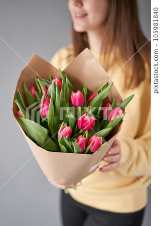 Crimson color tulips in woman hand. Spring bouquet of red tulips in hands. Bunch of fresh cut spring flowers 105981840