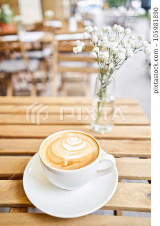Cup of hot cappuccino. The table in the coworking space of the coffee shop. A cup of coffee on the veranda on a sunny day. Coffee break at the cafe. Close-up 105981890