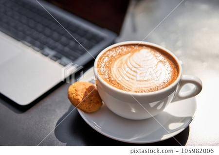 A man drinks coffee, holds a cup of hot Peanut latte in his hand. The table in the coworking space of the coffee shop. A cup of coffee on the veranda on a sunny day. Coffee break at the cafe. Close-up A man drinks coffee, holds a cup of hot Peanut latte in his hand. The table in the coworking space of the coffee shop. A cup of coffee on the veranda on a sunny day. Coffee break at the cafe. Close-up 105982006