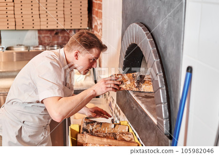 The chef prepares pizza in a neapolitan pizzeria. Cook in a apron in the kitchen with a shovel in his hands. boxes for food delivery on background. 105982046