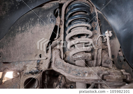 A car mechanic inspects springs, shock absorbers and suspension with a flashlight. Car on a repair stand. Technical service station for car. A car mechanic inspects springs, shock absorbers and suspension with a flashlight. Car on a repair stand. Technical service station for car. 105982101
