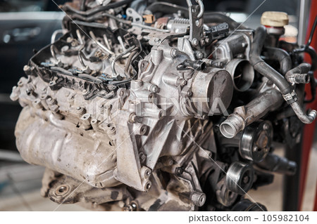 A car mechanic inspects the engine with a flashlight. Engine Block on a repair stand with Special crane jack. Technical service station for car. 105982104