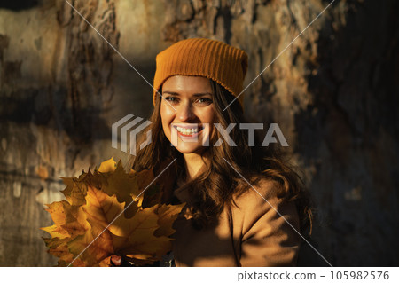 smiling elegant female in brown coat and hat against huge tree smiling elegant female in brown coat and hat against huge tree 105982576