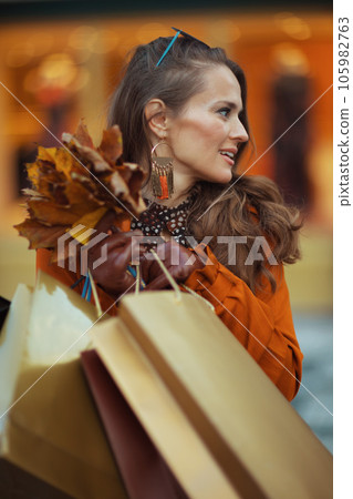 young woman in brown trench coat with shopping bags 105982763