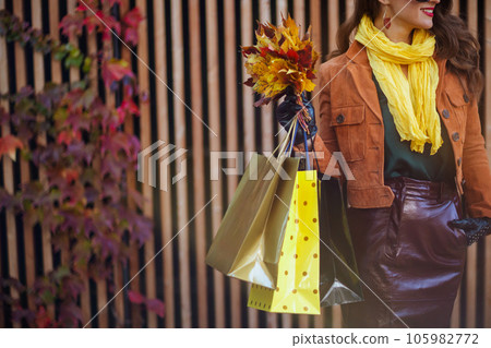 smiling young female in orange trench coat with shopping bags 105982772
