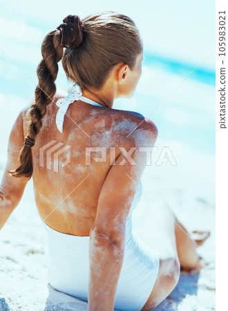 Young woman in swimsuit sitting on sandy beach and sunbathing 105983021