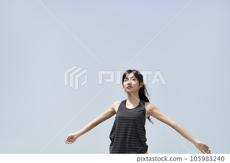 young asian woman in sportswear standing outdoors against blue sky with open arms young asian woman in sportswear standing outdoors against blue sky with open arms 105983240