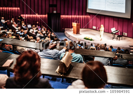 Business and entrepreneurship symposium. Female speaker giving a talk at business meeting. Audience in conference hall. Rear view of unrecognized participant in audience. Business and entrepreneurship symposium. Female speaker giving a talk at business meeting. Audience in conference hall. Rear view of unrecognized participant in audience. 105984591
