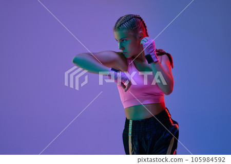 Teen athletic girl, MMA fighter in motion, training kicks against purple studio background in neon lights Teen athletic girl, MMA fighter in motion, training kicks against purple studio background in neon lights 105984592