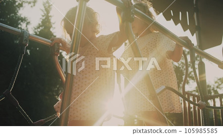 Two little sisters wearing similar dresses walk on a sunny park playaground 105985585